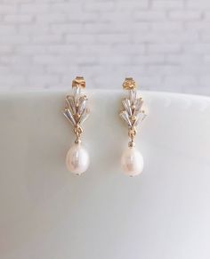 a pair of gold earrings with pearls and crystals on top of a white plate in front of a brick wall