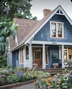 a blue house with lots of flowers in the front yard and landscaping on the side