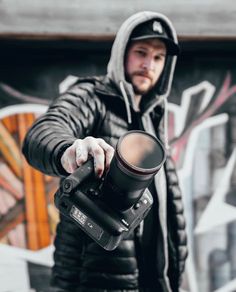 a man holding a camera in front of a wall with graffiti on it's walls