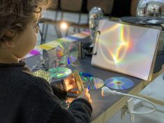 a young child is playing with cds on a table in front of other items and lights