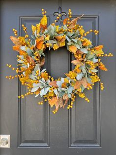 a wreath with yellow flowers and green leaves hanging on a gray front door, next to a black door