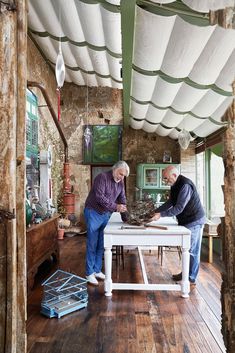 two men standing at a white table in a room with wood floors and ceilinging