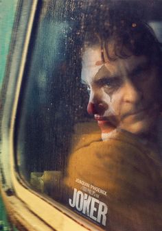 the joker movie poster is reflected in a car's side window as he looks out