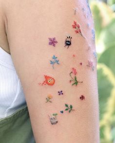 a woman's arm with colorful tattoos on her left shoulder and flowers in the background