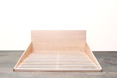 a wooden bed frame sitting on top of a cement floor next to a white wall