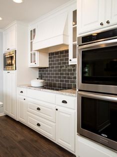 a kitchen with white cabinets and black tile backsplash, stainless steel appliances and wood flooring