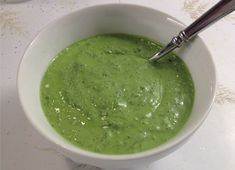 a white bowl filled with green soup on top of a table next to a spoon