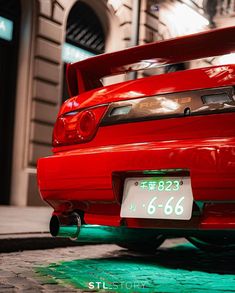 the back end of a red car parked in front of a building