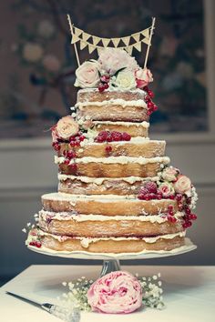 a three tiered cake with flowers and bunting on top is sitting on a table