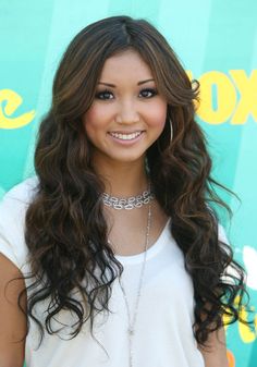 a beautiful young lady with long dark hair wearing a white shirt and silver necklace smiling at the camera