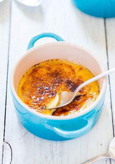 a blue pot filled with food on top of a white wooden table next to a spoon