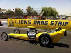 a yellow race car on the track with lions drag strip banner behind it's wheels