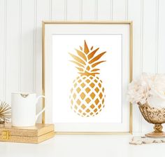 a gold pineapple art print on a white wall next to a vase with flowers