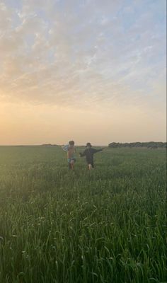 two young boys running through a field at sunset