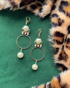 These gorgeous and unique statement hoops were designed in the art deco style of the 1920's. These are the perfect earrings for dressing up your holiday attire.These hoop earrings hang approximately 3.5" from the lobe and measure approximately 1.25" inches at their widest point. The design contains 12mm faux pearls, 4mm faux pearls, 3mm malachite heishi beads, and gold plated brass components.The leverback closure is 22k gold plated and should be suitable for sensitive ears. These are semi-light Brass Components, Holiday Attire, Heishi Beads, Art Deco Inspired, Hoop Art, Sensitive Ears, Art Deco Style, 22k Gold, Deco Style