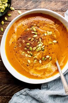 a white bowl filled with carrot soup and topped with pistachio seeds, on top of a wooden table