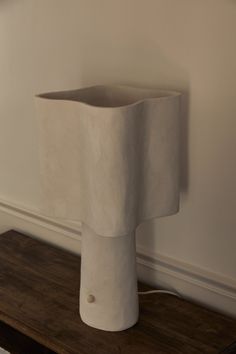 a large white vase sitting on top of a wooden table next to a lamp shade