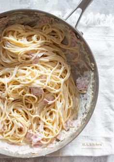 a pan filled with pasta and ham on top of a white cloth next to a fork