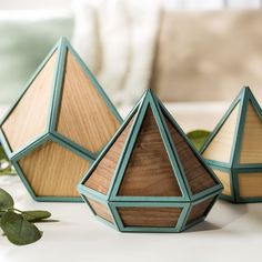 three wooden geometric shapes sitting on top of a white table next to green planters