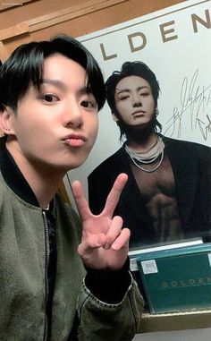 a young man making the peace sign in front of a poster