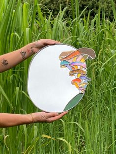 a person holding up a mirror in the middle of some tall grass with an image on it