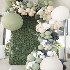 an arrangement of balloons and greenery is displayed in front of a wall with white flowers