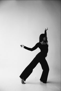 a woman in black is dancing with her arms outstretched and legs bent forward, on a white background