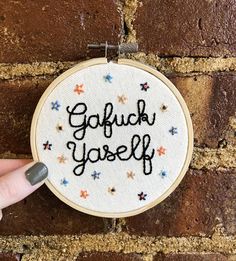 someone is holding up a hand embroidered hoop with the words gaffuck yourself on it