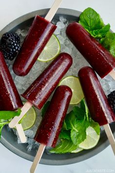 three popsicles with limes, blackberries and mint leaves on a platter