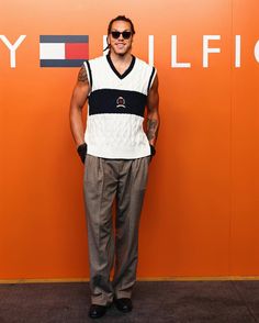 a man standing in front of an orange wall with his hands on his hips wearing sunglasses