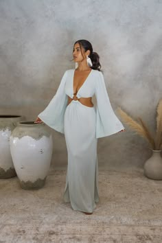 The KEHLANI CUT-OUT DRESS is a floor-length dress designed with a plunging-v neckline and elegant side cut-outs that shape your figure and are fastened at the center with a bamboo ring to flatter. Kehlani features full-length bell sleeves and knee-high slits on either side, and is cut from our viscose crinkle crepe fabric for a sexy, lightweight feel. Resort Style Photoshoot, Beach Outfits Women Vacation Resort Wear Summer Dresses, Desert Photoshoot Outfit, Dubai Ideas, Minimal Portrait, Soft Feminine Outfits, Pajamas Aesthetic, Classy Wardrobe, Greece Fashion