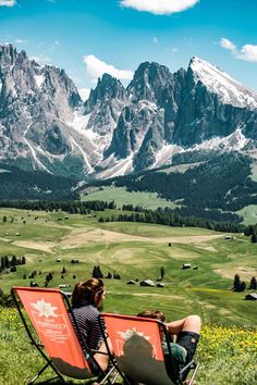 a woman sitting in a chair on top of a grass covered field next to mountains