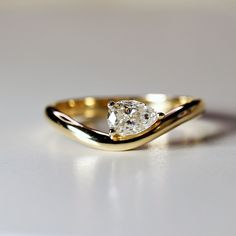 a gold ring with a single diamond on it's side, sitting on a white surface