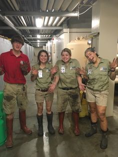 four people in green shirts and brown shorts posing for the camera with their hands up