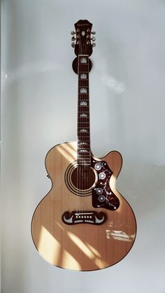 an acoustic guitar hanging from the wall in a room with white walls and shadows on it