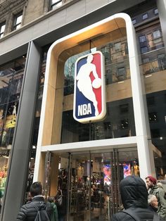 people are walking in front of a building that has a basketball logo on the door