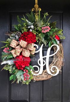 a wreath with the letter h on it hanging from a front door decorated with greenery and red flowers