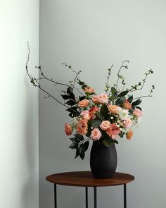 a black vase filled with pink and white flowers on top of a small wooden table