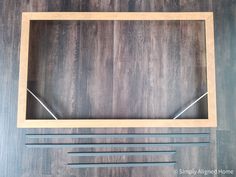 an empty wooden shelf with metal handles on a wood floor next to some scissors and tape