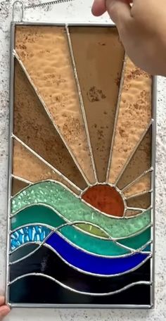 a hand holding a stained glass window with waves and sun in the middle, on a white wall