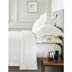 a bed with white sheets and pillows next to a small side table on the floor