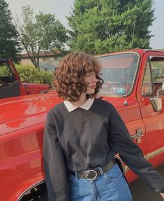 a woman standing in front of a red truck with her hand on the door handle