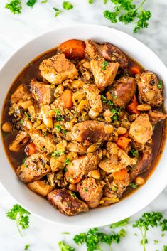 a white bowl filled with chicken and carrots on top of a marble countertop