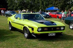 a bright yellow car parked on top of a lush green field next to other cars