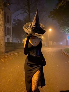 a woman in a witch costume is walking down the street at night with her hat on