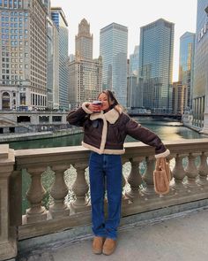 a woman standing on a bridge taking a photo with her cell phone in the city