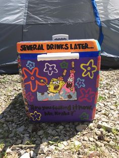 a cooler sitting on top of a gravel ground next to a blue and black tent