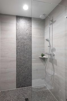 a walk in shower sitting next to a tiled wall and floor covered in grey tiles