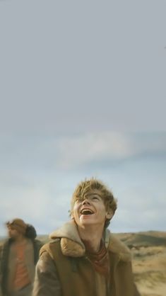 two people walking in the sand with one person laughing and another looking up at something