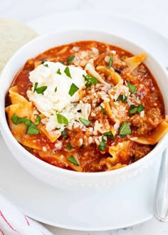 a white bowl filled with pasta and cheese on top of a plate next to bread